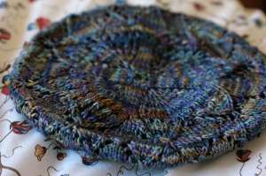 A lacy beret, with blue and purple yarn, on a flowery bedspread
